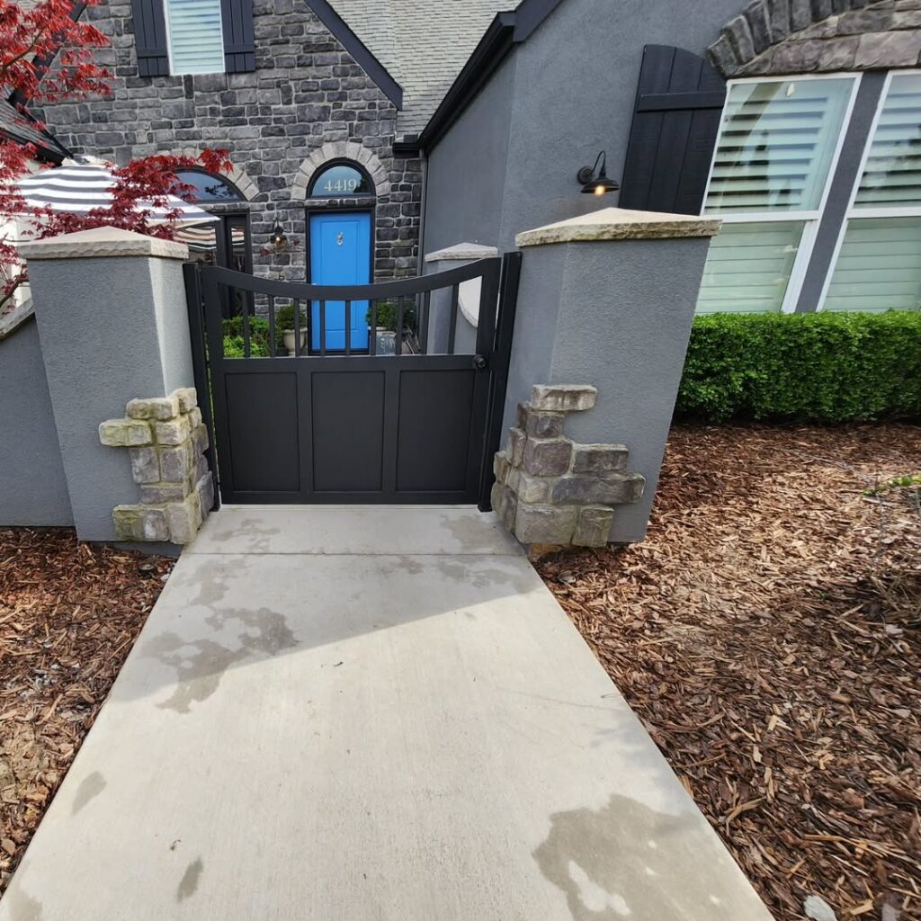 Steel entry gate between stone columns on a concrete path