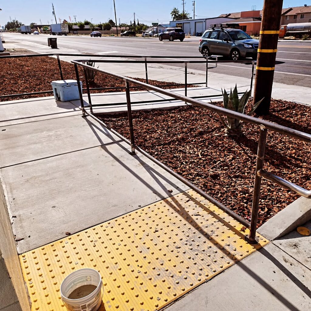 Handrail beside a ramp with tactile paving at a commercial entrance