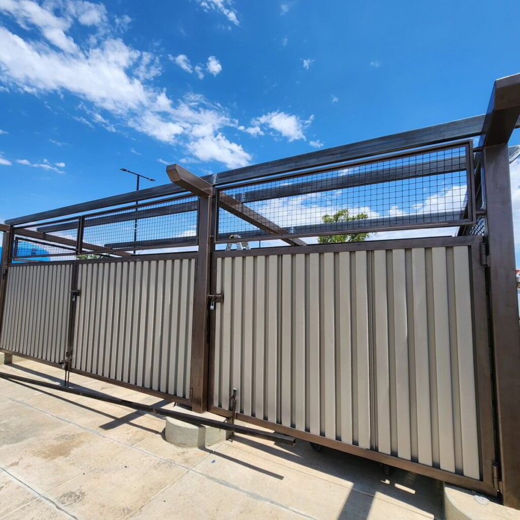 Dark metal gate and corrugated fence panel against a blue sky